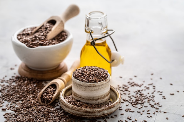 Óleo de linhaça em uma garrafa e tigela de cerâmica com sementes de linhaça marrons e colher de pau em um branco