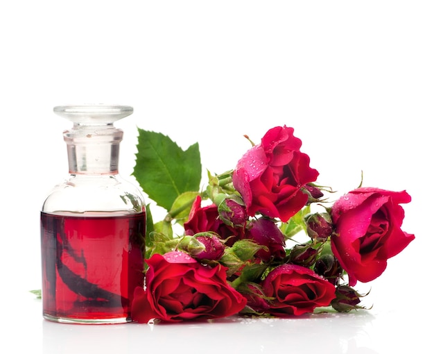 Óleo de massagem de rosas em uma garrafa de vidro e flores rosas em um fundo branco