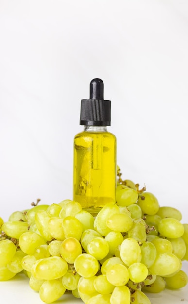 Óleo de semente de uva em uma garrafa de vidro com uma pipeta e uvas verdes sobre um fundo claro. Bio cosméticos orgânicos com ingredientes vegetais.