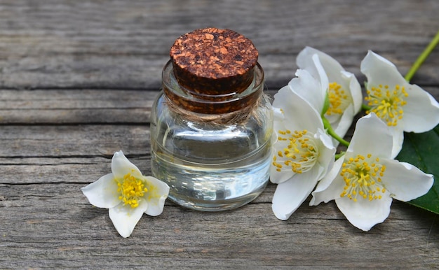 Óleo essencial de jasmim em uma garrafa de vidro e flores frescas de jasmim em fundo de madeira velho