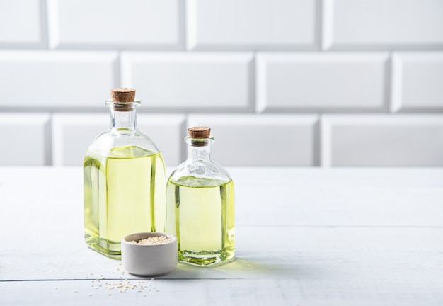 Óleo vegetal natural de sementes de gergelim em uma garrafa transparente na mesa da cozinha branca. Alimentos dietéticos saudáveis. Vista frontal e espaço de cópia