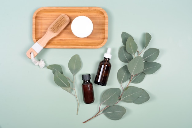 Óleos essenciais, recipiente para creme facial e escova de massagem com folhas naturais de eucalipto sobre fundo verde
