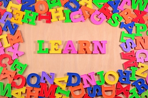 Lernen Sie, mit bunten Plastikbuchstaben auf einem hölzernen Hintergrund geschrieben