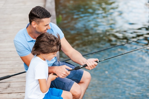 Lernen vom Profi. Draufsicht auf Vater und Sohn beim Angeln am Flussufer