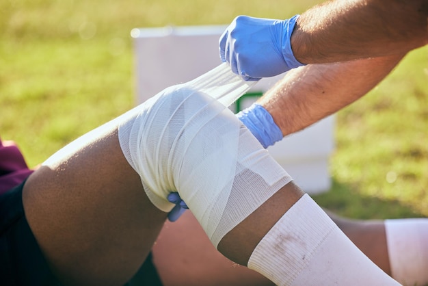 Foto lesão esportiva de primeiros socorros e bandagem de perna com acidente de futebol, fitness e massagem em um campo treino de treinamento e fisioterapia de dor no joelho em jogo com emergência de saúde devido ao exercício