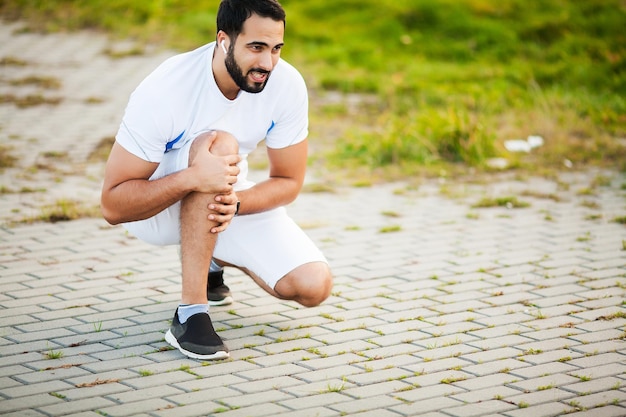 Lesão na perna. Atleta do sexo masculino que sofre de dor na perna durante o exercício ao ar livre.