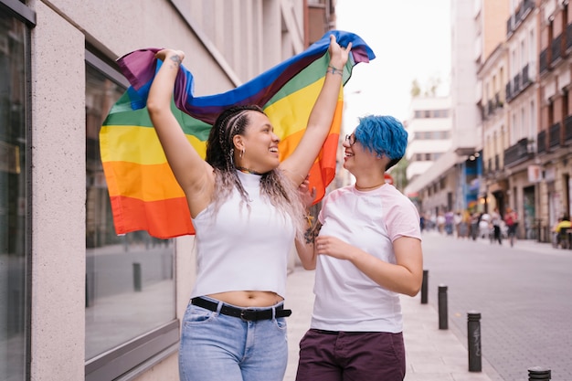 Lesbenpaar mit verspielter haltung, die stolz eine stolz-lgbt-flagge zeigt.