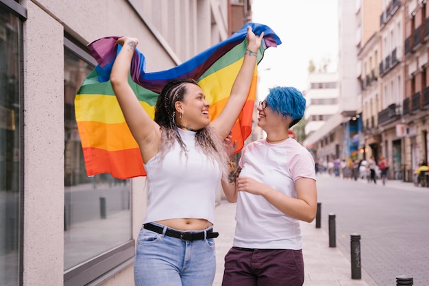 Lesbenpaar mit verspielter Haltung, die stolz eine Stolz-lgbt-Flagge zeigt.