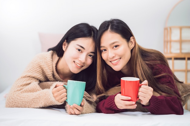 Lesbenpaarliebhaber der jungen schönen asiatischen Frauen, die Kaffeetasse im Schlafzimmer zu Hause halten.