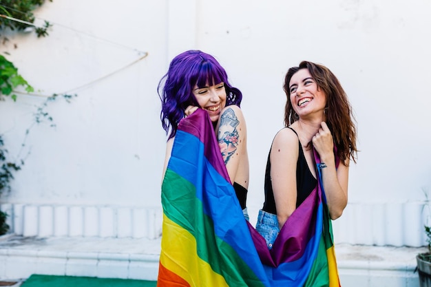 Lesbianas sonrientes sosteniendo la bandera del arco iris al aire libre