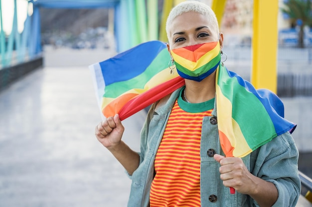 Lesbische Frau mit Gay-Pride-Maske, während sie die LGBT-Regenbogenflagge hält - Fokus auf Gesicht