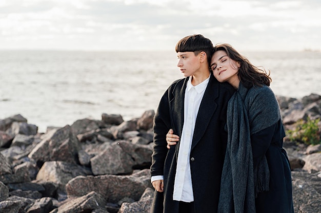 Lesbische Frauen umarmen sich, während sie auf einem Felsen gegen Meer und Himmel stehen