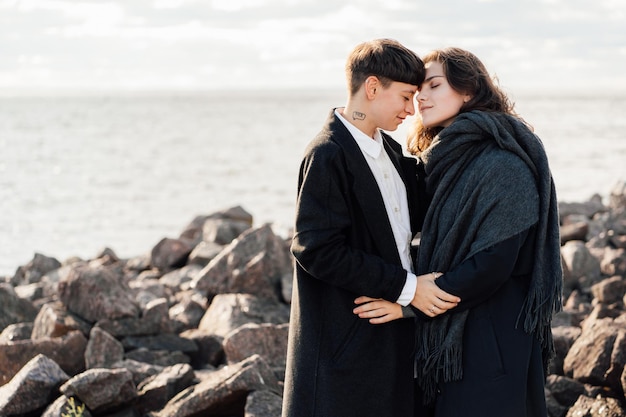 Lesbische Frauen umarmen sich, während sie auf einem Felsen gegen Meer und Himmel stehen