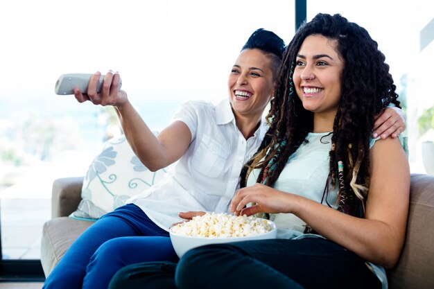 Lesbische Paare, die auf Sofa sitzen und mit einer Schüssel Popcorn fernsehen