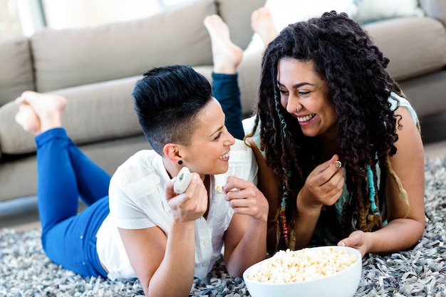 Lesbische Paare, die auf Wolldecke mit einer Schüssel Popcorn und Fernbedienung liegen