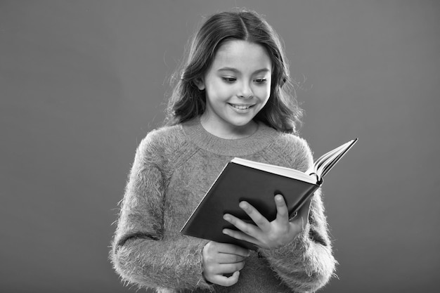 Leseaktivitäten für Kinder Mädchen halten Buch lesen Geschichte über orangefarbenen Hintergrund Kind lesen gerne Buch Buchladenkonzept Wunderbare kostenlose Kinderbücher zum Lesen von Kinderliteratur