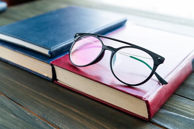 Lesebrille auf Hardcover-Bücher über Holztisch aufsetzen