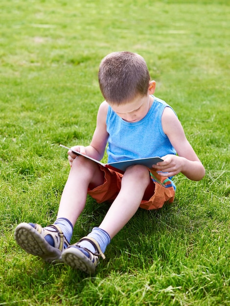 Lesebuch des kleinen Jungen outdoori auf Gras