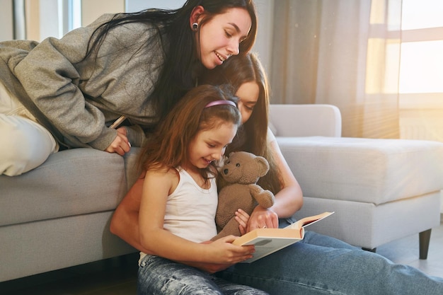 Lesebuch zusammen Weibliches lesbisches Paar mit kleiner Tochter, die Zeit zusammen zu Hause verbringen