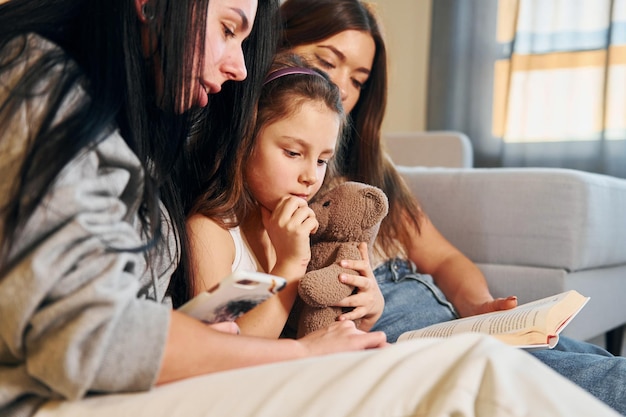 Lesebuch zusammen Weibliches lesbisches Paar mit kleiner Tochter, die Zeit zusammen zu Hause verbringen
