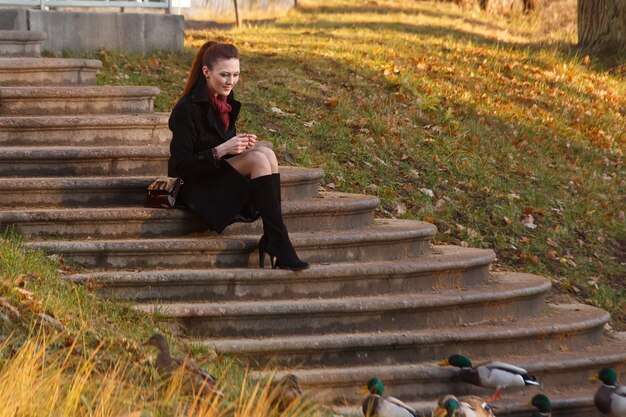 Lesekopfmädchen sitzt auf der Steintreppe und füttert Enten im Herbstpark