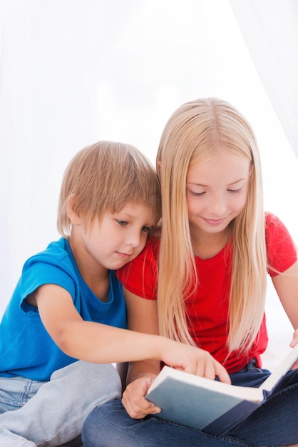 Lesen ihres Lieblingsbuches. Zwei süße Kinder, die zusammen ein Buch lesen, während sie zusammen auf dem Bett sitzen