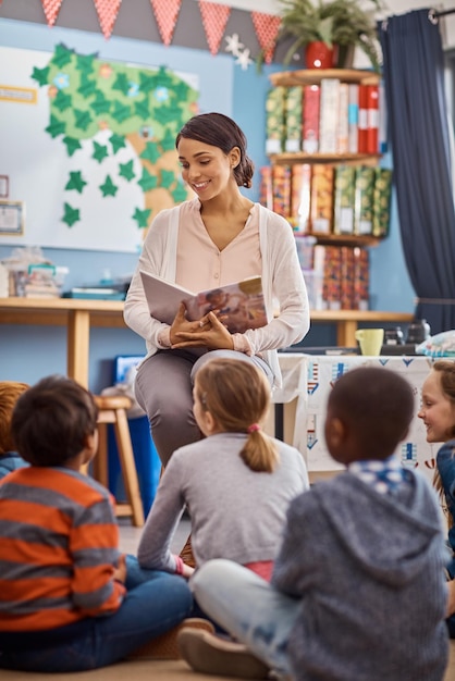 Lesen öffnet ihre Vorstellungskraft noch mehr Einstellung eines Lehrers, der einer Gruppe von Grundschulkindern im Unterricht vorliest