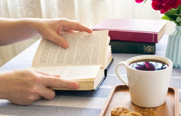 Lesen Sie ein Buch an einem Tisch am Fenster Buchen Sie in Handmorgenkaffee zu Hause oder in einer gemütlichen Atmosphäre eines Cafés