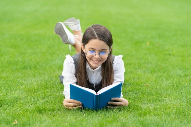 Lesezeit Glückliches Schulmädchen-Lesebuch, das nach der Schullesung auf Gras liegt