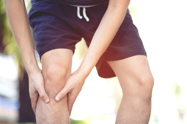 Lesión por concepto de entrenamiento: el hombre asiático usa las manos para sostener su rodilla mientras corre en la carretera en el parque