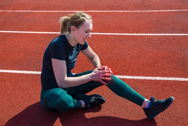 Lesión de rodilla deportiva. Mujer tiene dolor en la rodilla después de correr al aire libre en el estadio