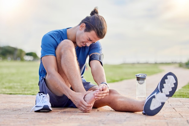 Foto lesiones deportivas y dolor de pies con un hombre en el parque por inflamación de espasmos musculares y problemas articulares entrenamiento y ejercicio con atletas y emergencias por problemas de salud y tobillo roto