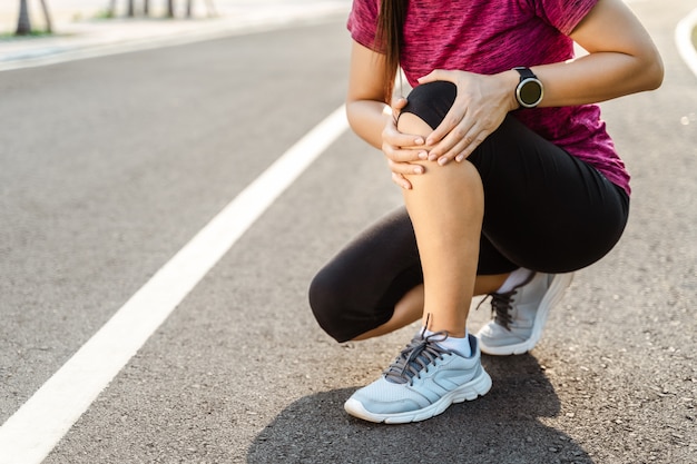 Lesiones de rodilla. Mujer deportiva con fuertes piernas atléticas sosteniendo la rodilla con las manos doloridas después de sufrir una lesión muscular durante un entrenamiento de entrenamiento en Running Track. Concepto de salud y deporte.