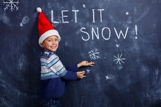 Let It is Snow Boy com chapéu de Papai Noel com neve pintada em estúdio