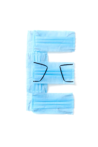 Letra mayúscula E hechos a mano de máscaras faciales azules protectoras antibacterianas médicas sobre una pared blanca, espacio de copia. Alfabeto creativo para inventar nuevas palabras.