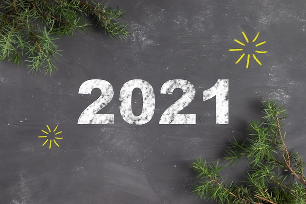 Foto letras de 2021 con tiza sobre una pizarra gris con ramas de abeto