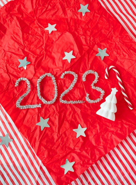 Letras 2023 de lluvia de guirnaldas brillantes sobre fondo rojo con estrellas de papel de regalo Decoración de Año Nuevo y Navidad Dulces de Navidad y árbol de Navidad decorativo en el fondo