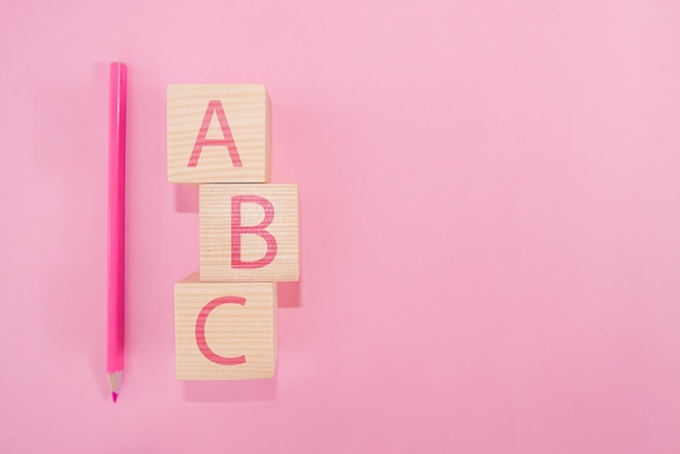 Letras ABC do alfabeto em blocos cúbicos de madeira na forma de um pilar com um lápis rosa em um fundo rosa. Copie o espaço. Conceito de escola.