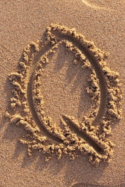 Letras del alfabeto (Q) escritas a mano en la arena de la playa