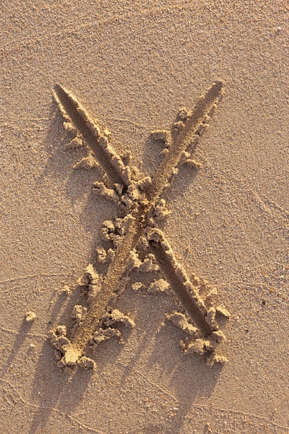 Letras del alfabeto (X) escritas a mano en la arena de la playa