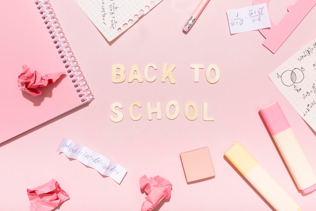 Letras de volta à escola em um fundo rosa com material escolar