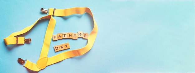 Foto letras del día del padre feliz hechas con cubos de madera sobre un fondo azul con tirantes amarillos