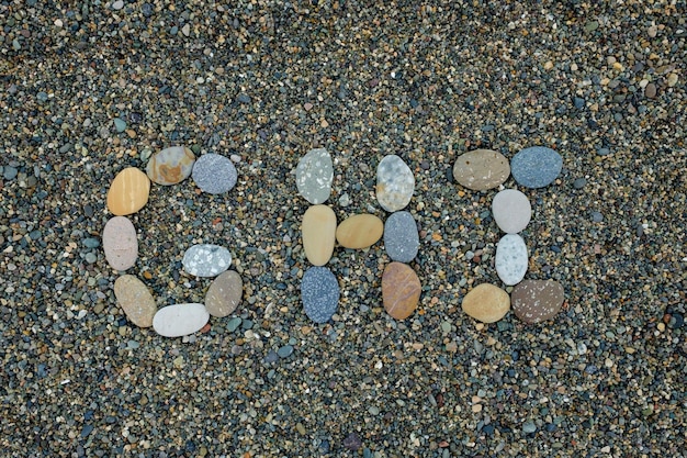 Letras ghi hechas de piedras en arena en la playa