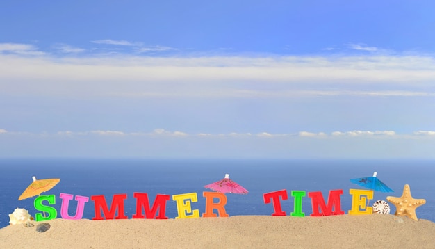 Letras de horario de verano en la arena de una playa con el fondo del mar