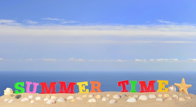 Letras de horario de verano en la arena de una playa con el fondo del mar