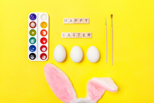 Letras con huevos, pinturas de colores y orejas de conejo aisladas sobre fondo amarillo