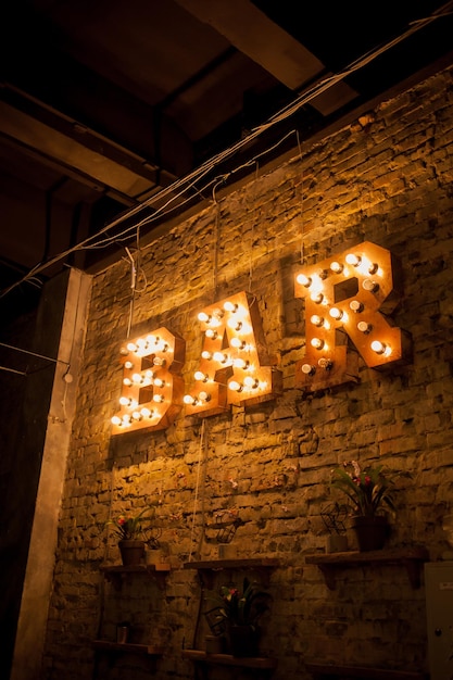 Foto letras luminosas bar letras volumétricas bar de metal enferrujado em uma parede de tijolos