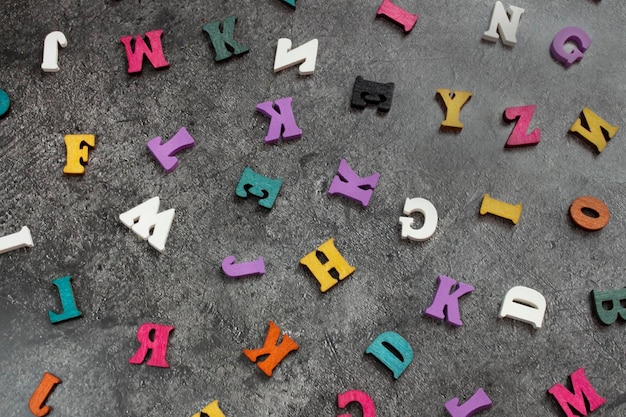 Letras de madera multicolores del alfabeto inglés sobre un fondo de hormigón oscuro Un patrón de letras del alfabeto Muchas letras de madera