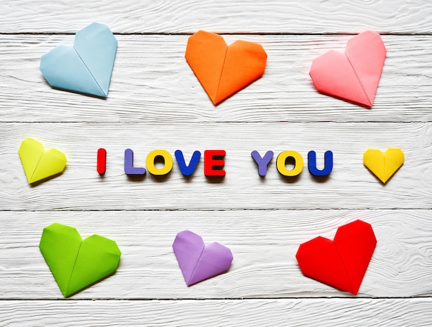 Letras de madera multicolores que componen la inscripción te amo y corazones de papel de origami multicolores en una madera blanca día de san valentín