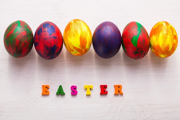 Letras de madera multicolores que componen las palabras felices pascuas y huevos coloridos decorativos sobre un fondo blanco con espacio de copia.